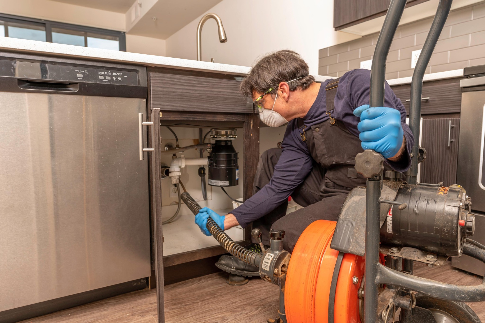 Plumber using a drain snake to unclog a kitchen sink.